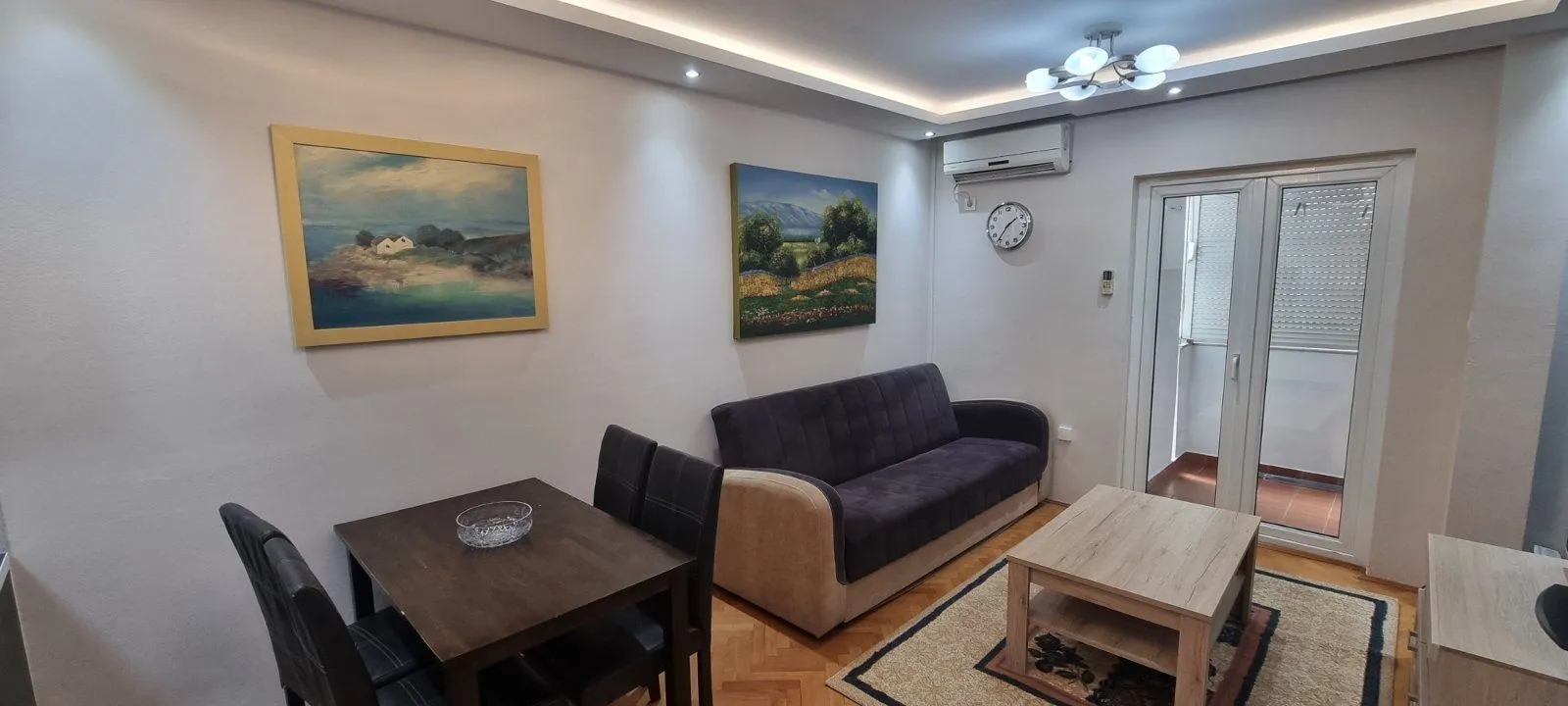 Svijetla dnevna soba sa kaučem, trpezarijskim stolom i umjetničkim slikama na zidu.