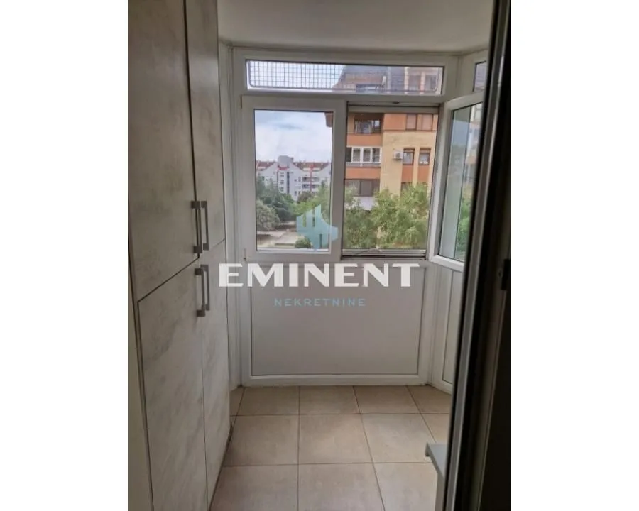 Zastakljeni balkon sa ugradnim ormarom i pogledom na okolne zgrade.