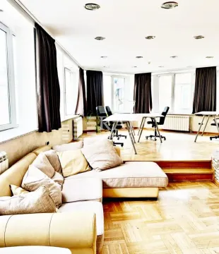 Spacious living room with a sofa and office desks in the background. - image 7