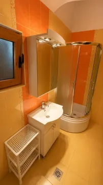 Kupatilo sa tuš kabinom, umivaonikom i bijelim elementima u narandžastim tonovima. - image 19