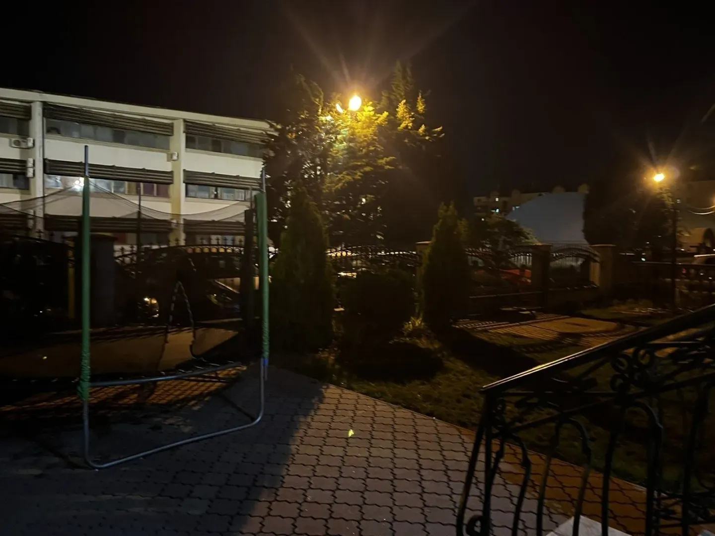 Dvorište zgrade noću sa popločanim dijelom i zelenilom.