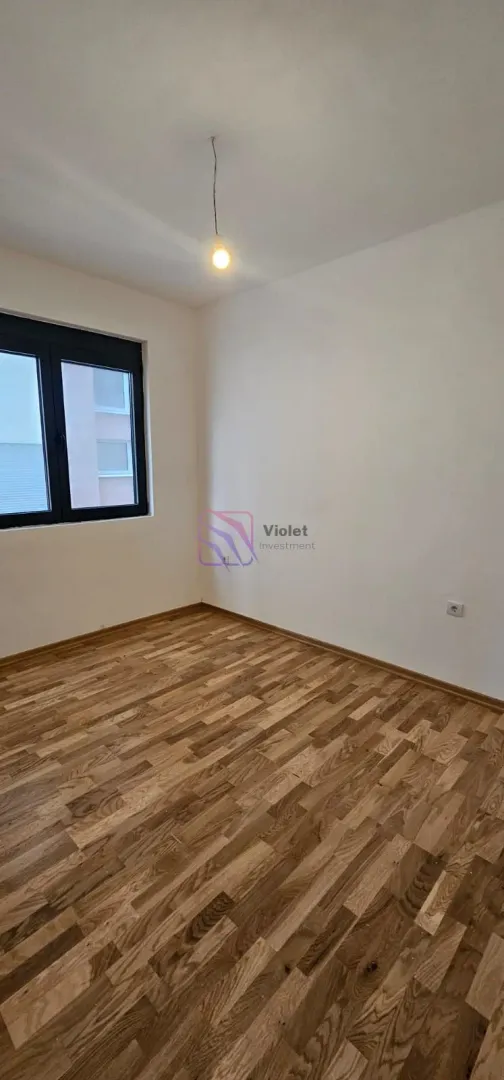 Prazna soba sa parketom na podu i jednim prozorom.