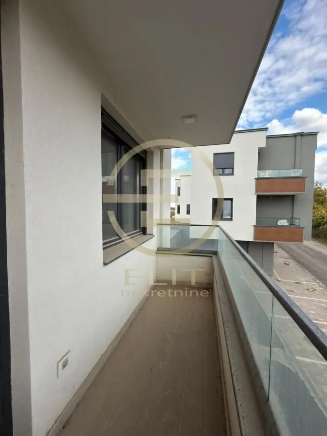 Pogled na prostrani balkon sa staklenom ogradom i pogledom na okolne zgrade.
