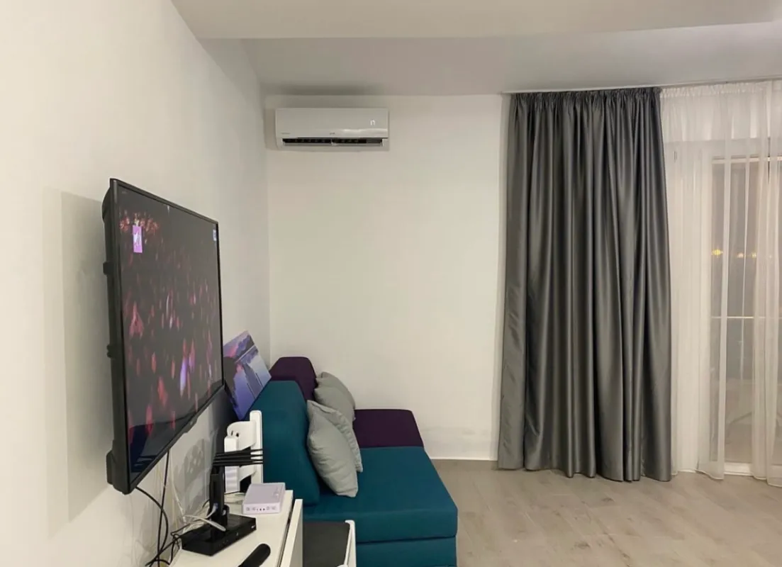 Dnevna soba sa garniturom, televizorom na zidu i klima uređajem.