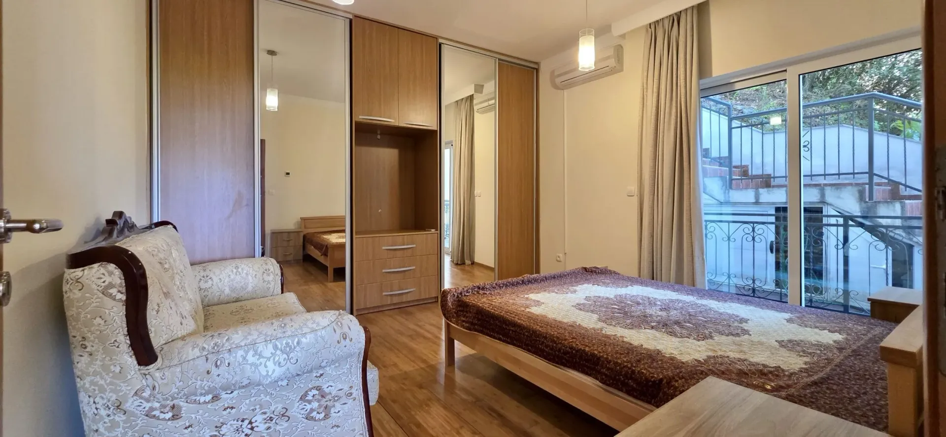 Namještena spavaća soba sa velikim garderoberom, krevetom i foteljom.