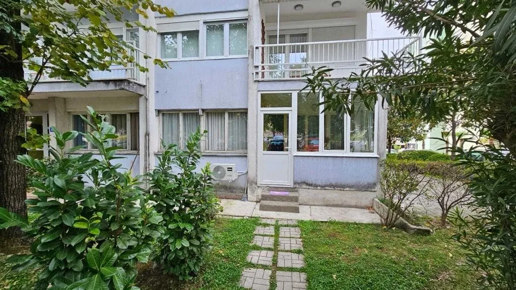 Pogled na ulaz i dvorište stambene zgrade sa zelenilom.