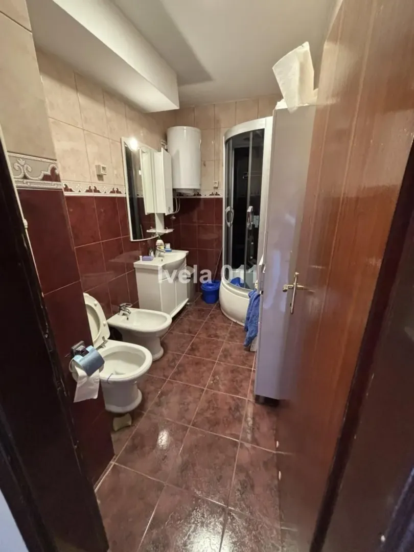 Kupatilo opremljeno sanitarijama, umivaonikom, tuš kabinom i pločicama u smeđim tonovima.