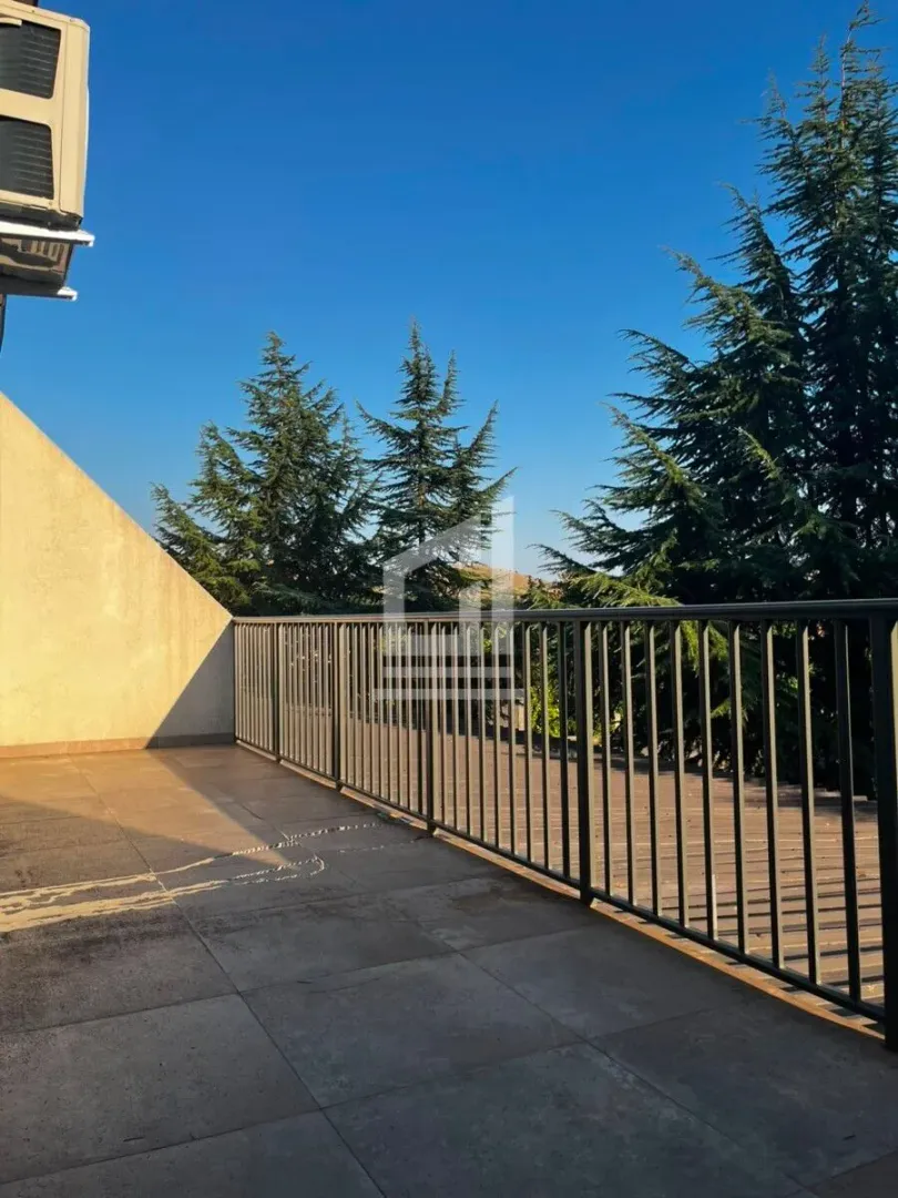 Spacious terrace with a metal railing and a view of greenery.