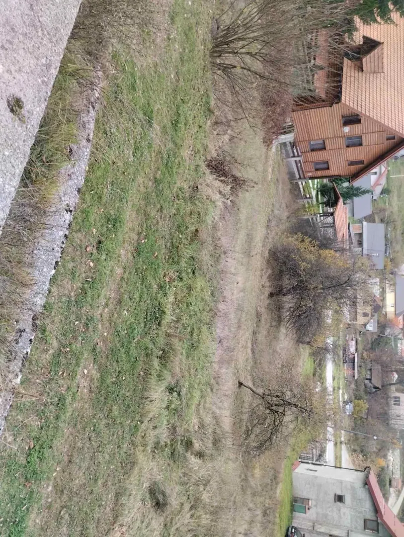 Zeleni travnati plac u planinskom naselju okružen brvnarama.