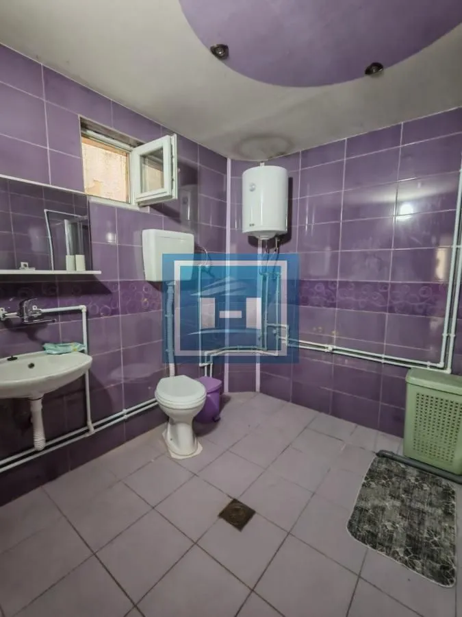 Kupatilo obloženo ljubičastim pločicama sa umivaonikom, WC šoljom i bojlerom.