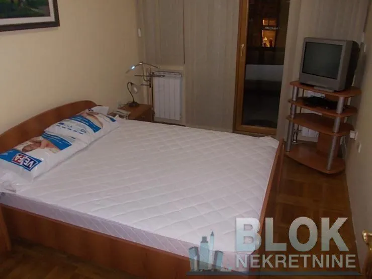Furnished bedroom with a double bed, bedside table, and television.