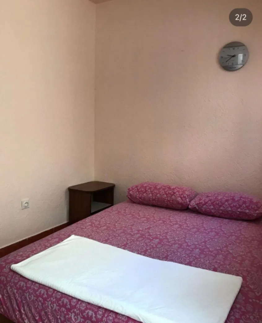 A bedroom with a double bed, a nightstand, and a wall clock.