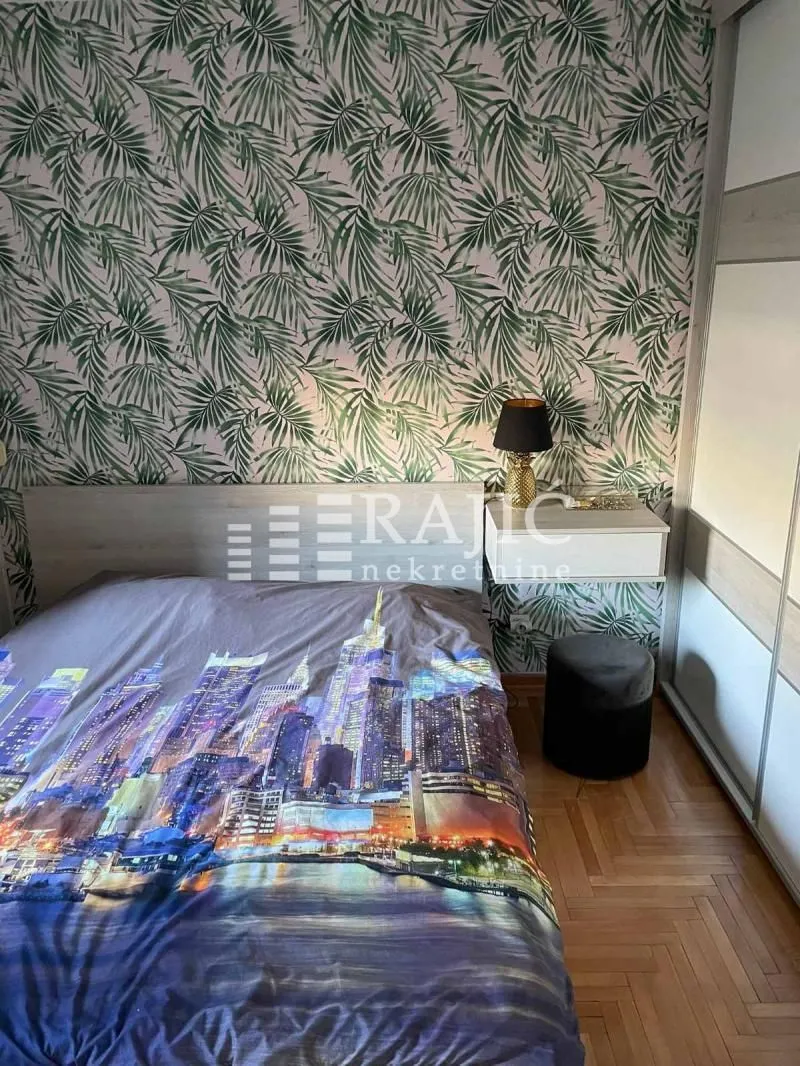 Furnished bedroom with a double bed and patterned wallpaper.