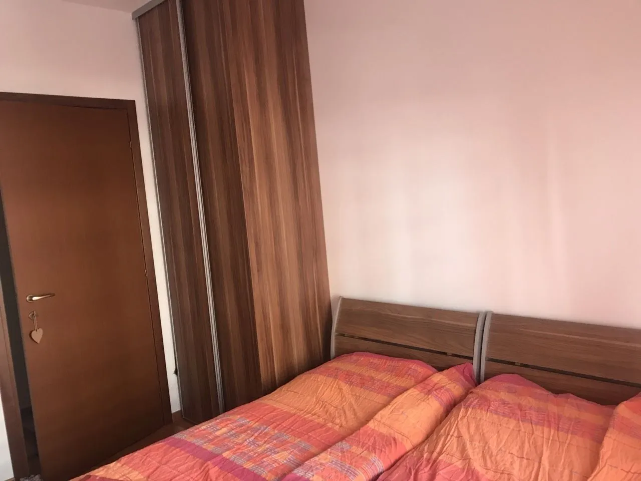 A bedroom with a double bed and a wooden wardrobe.