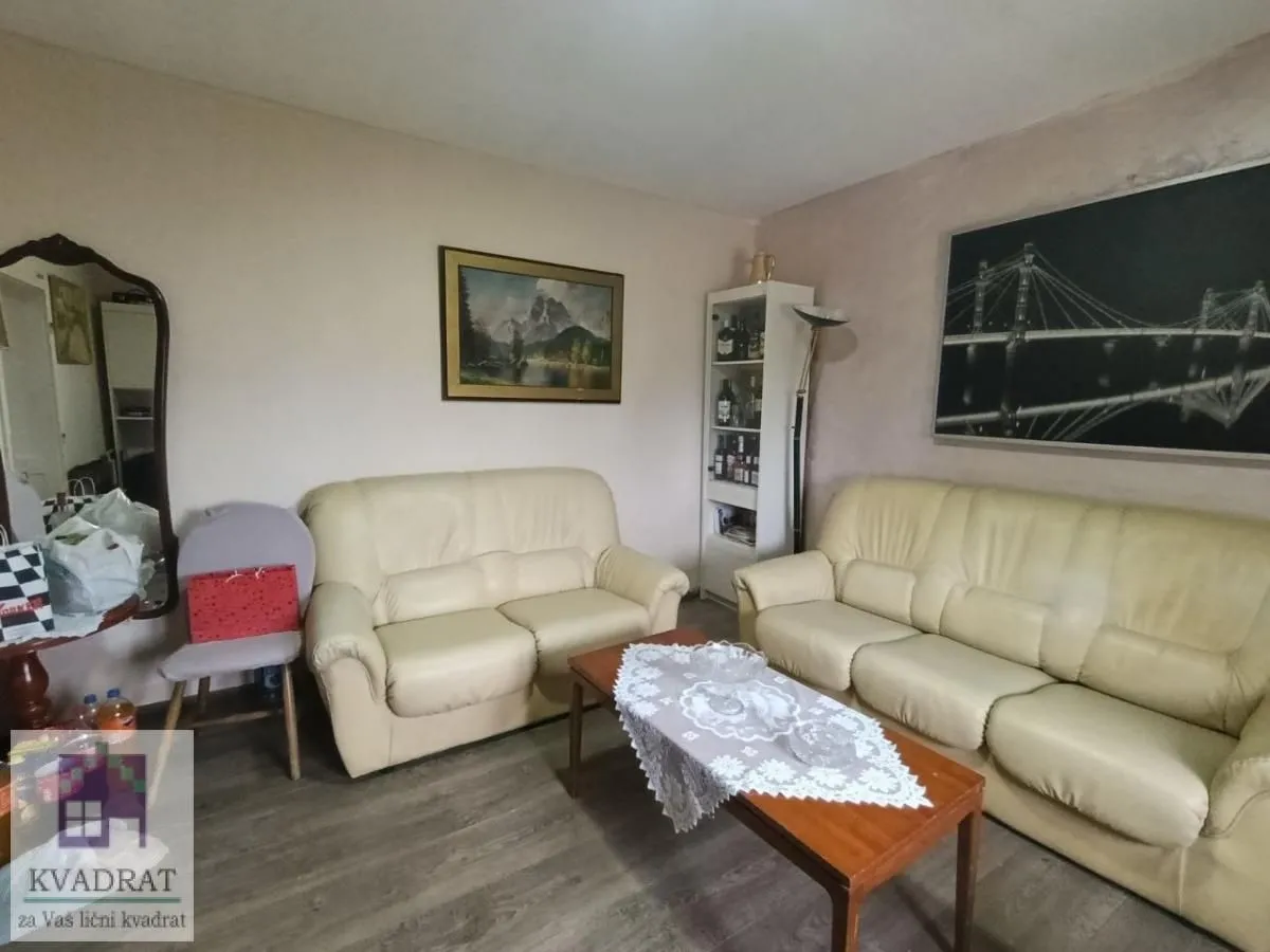Dnevna soba sa garniturom za sedenje, stočićem i slikama na zidu.