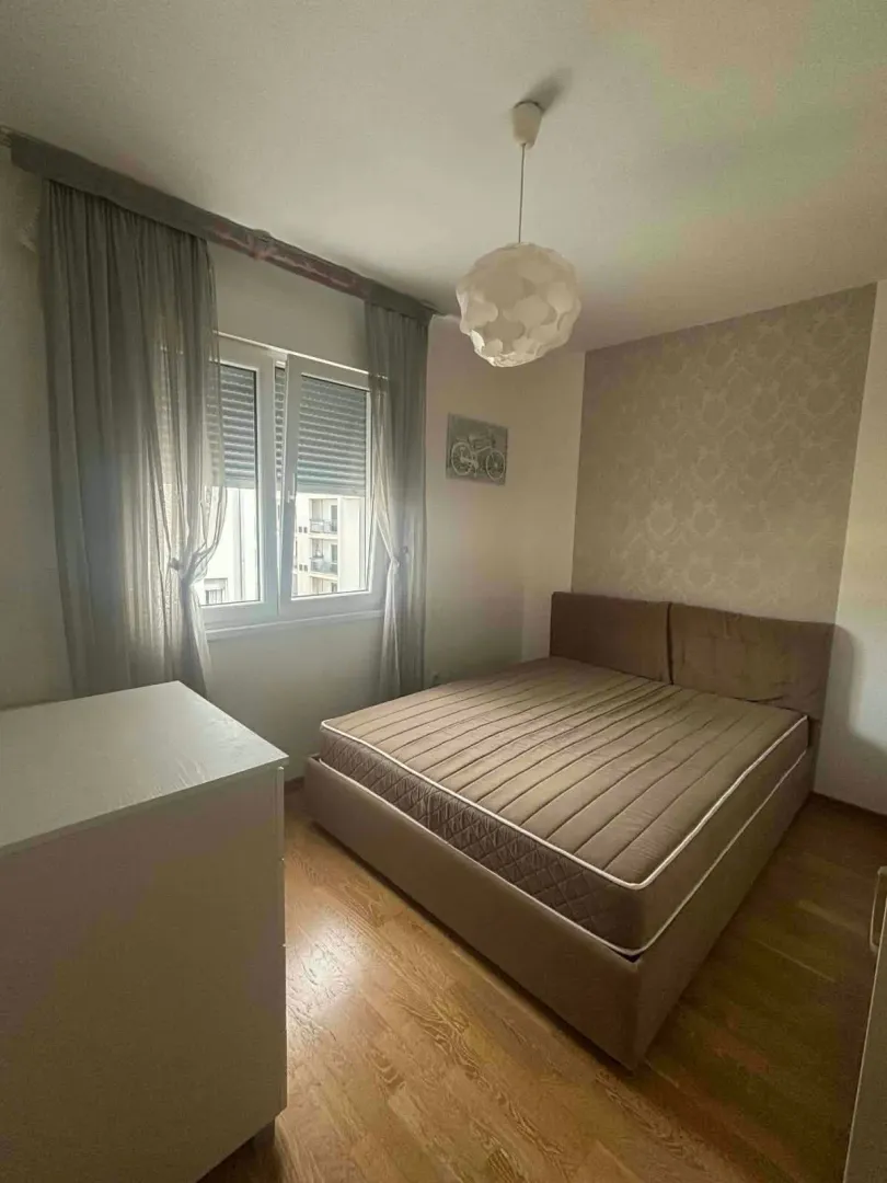 Spavaća soba sa bračnim krevetom, prozorom i komodom.