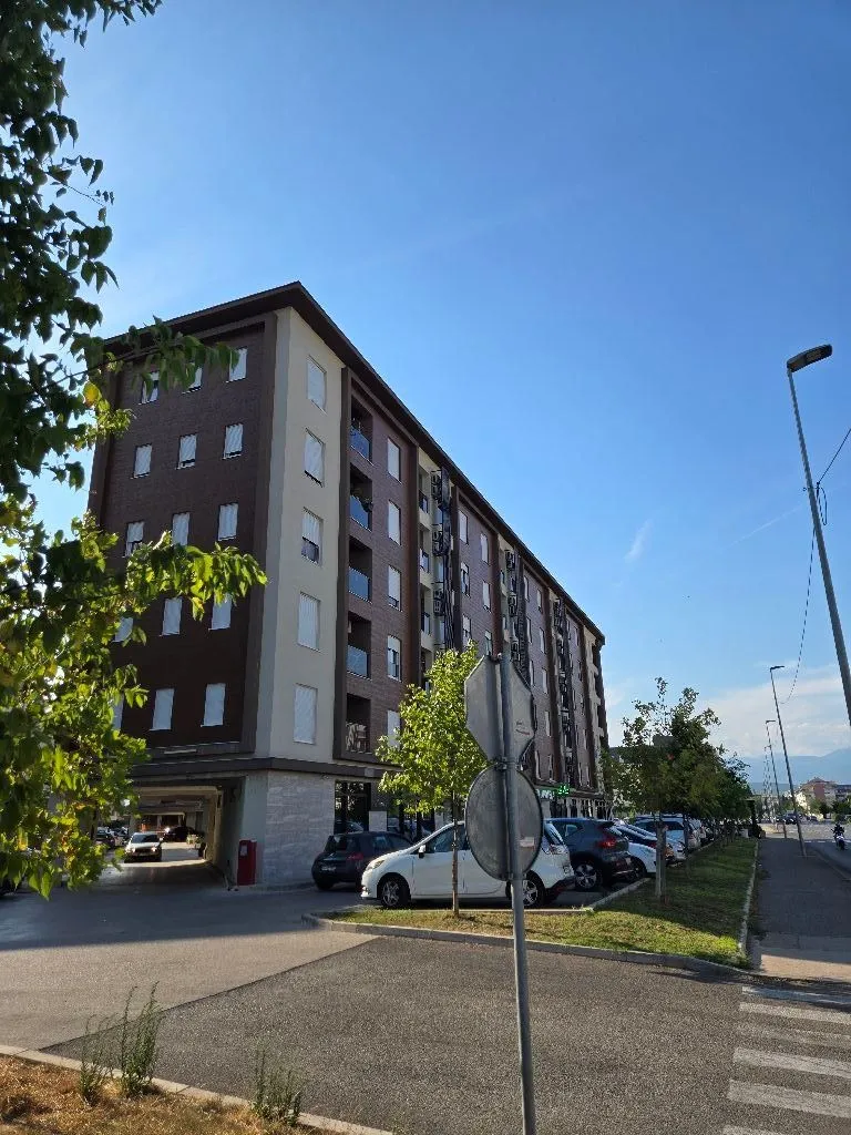 Spoljašnji izgled stambene zgrade sa parkingom i ulicom.