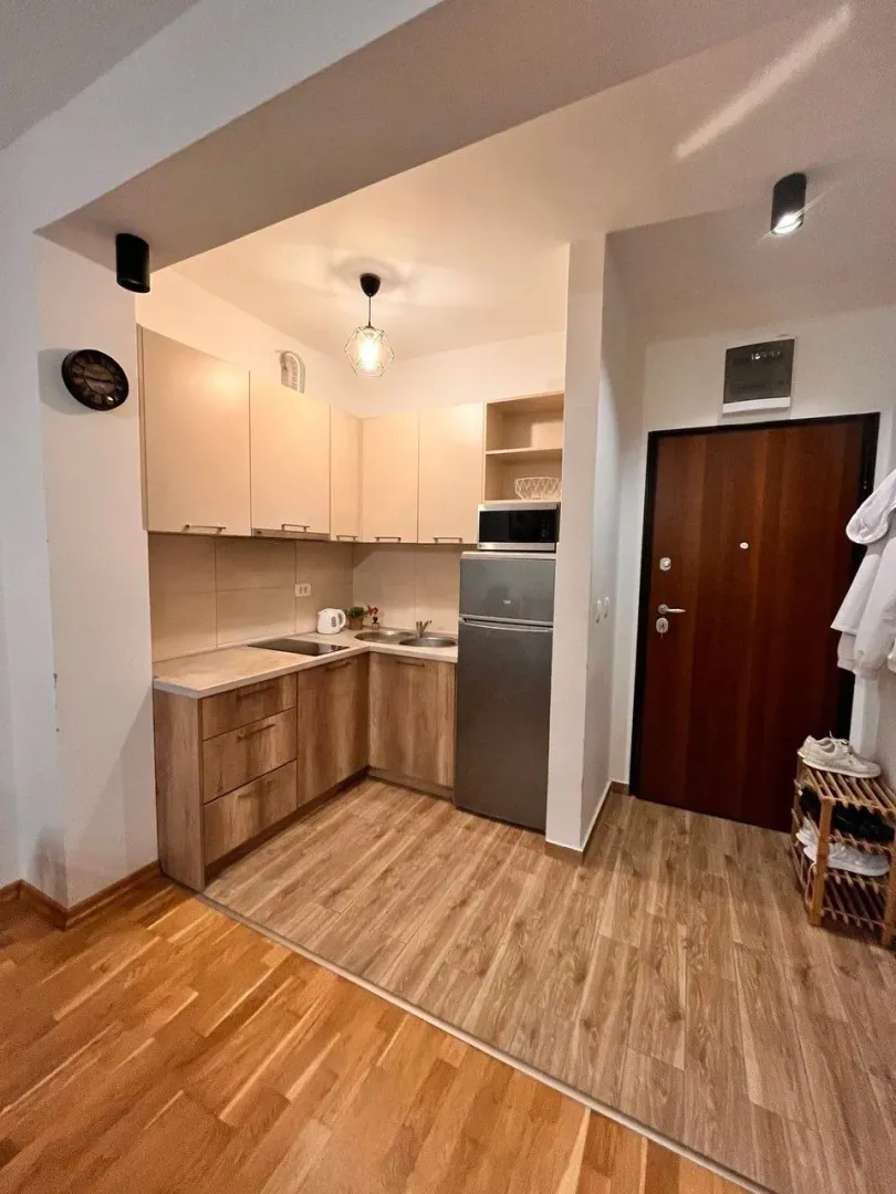 Manja kuhinja sa drvenim elementima i frižiderom u nastavku hodnika.