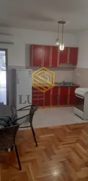 Manja kuhinja sa crvenim elementima i trpezarijskim stolom u prvom planu. - image 3