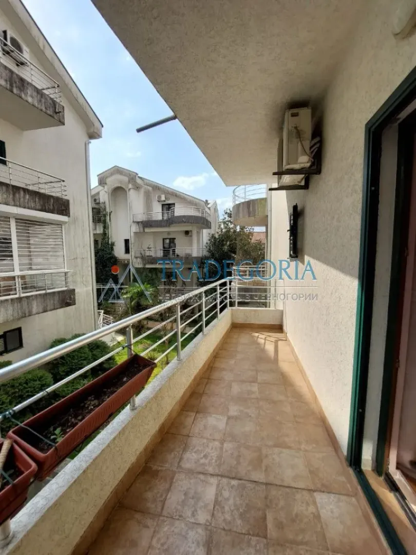 Dugačak popločani balkon sa metalnom ogradom i pogledom na okolne zgrade.