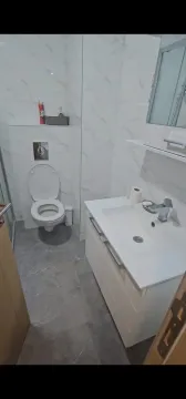 Modernly equipped bathroom with white tiles, a vanity unit, and a toilet. - image 8