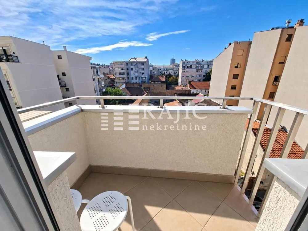 Small tiled balcony with a metal railing and a city view.
