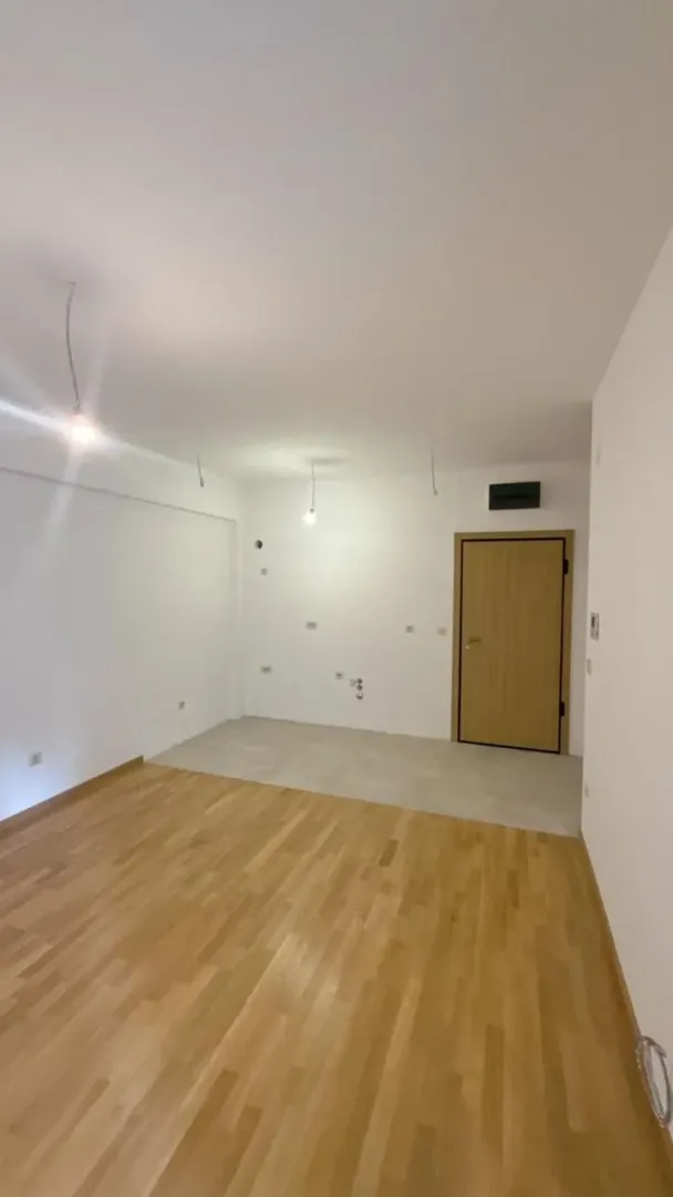Prazna prostorija sa drvenim podom, bijelim zidovima i drvenim vratima.