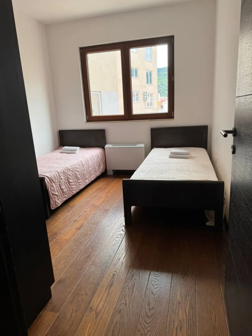 Bright bedroom with two single beds and wooden flooring.