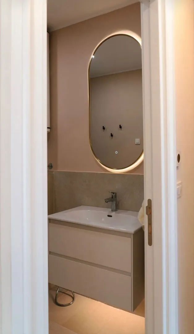 View of a modern bathroom with a vanity sink and lit mirror through an open doorway.