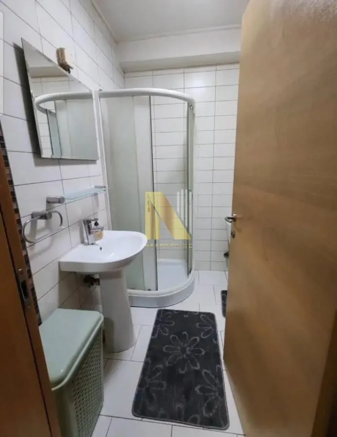 Manje kupatilo sa tuš kabinom, umivaonikom i ogledalom.
