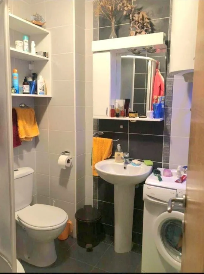 Manje kupatilo sa umivaonikom, wc šoljom, ormarićem sa ogledalom i veš mašinom.