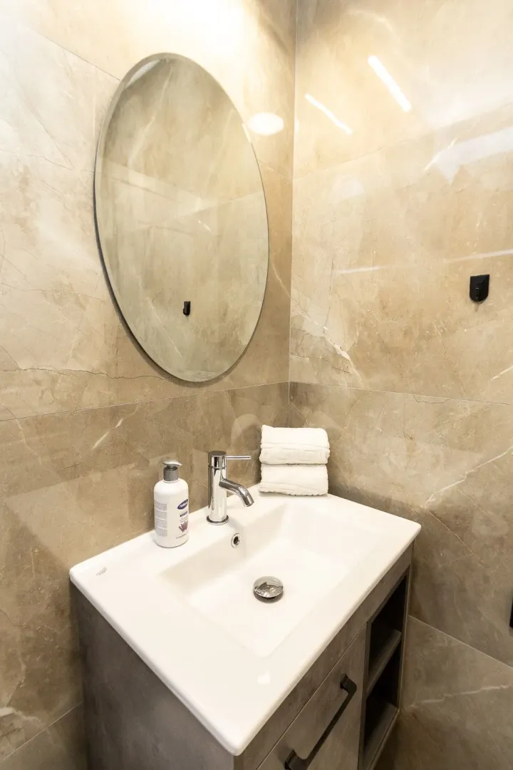 Modern bathroom with a sink, mirror, and beige tiles.