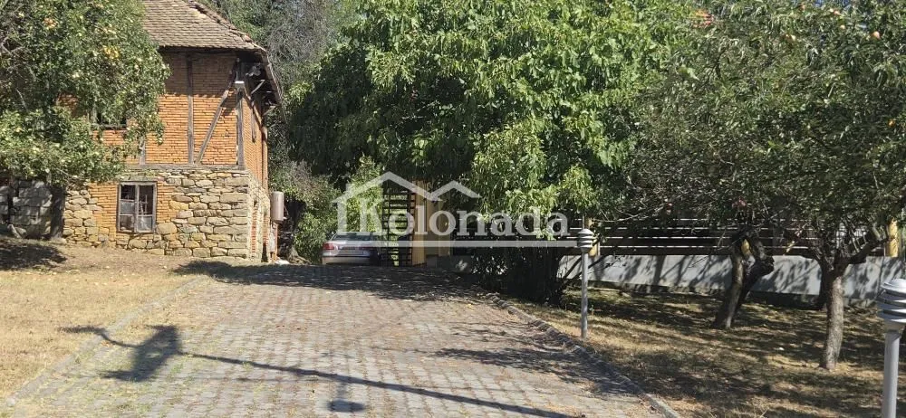 Dvorište sa prilazom i kućom u tradicionalnom stilu okruženom zelenilom.