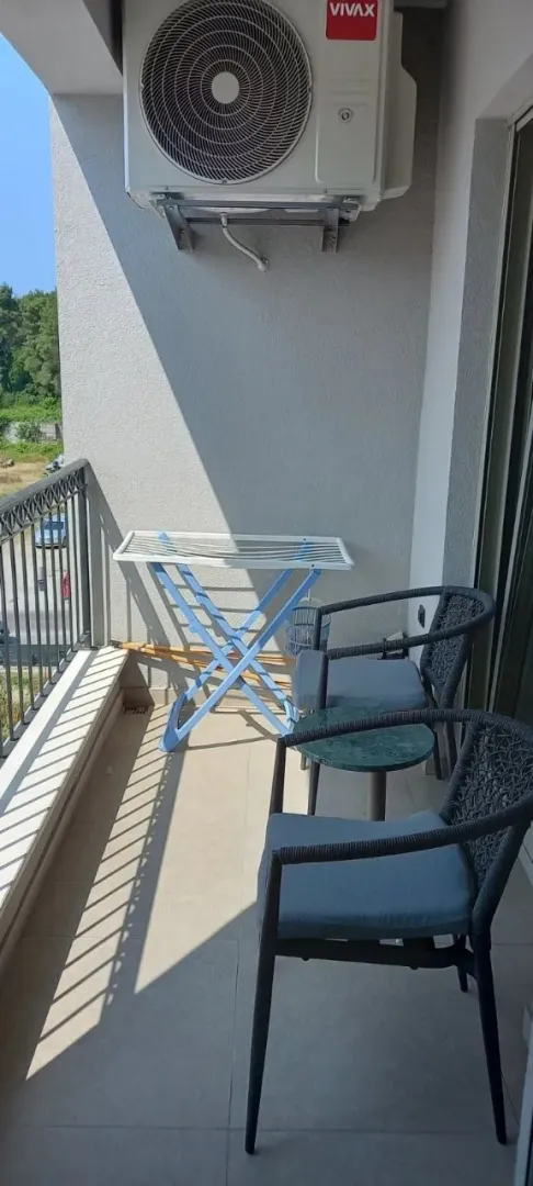 Small covered balcony with seating furniture and an air conditioner.