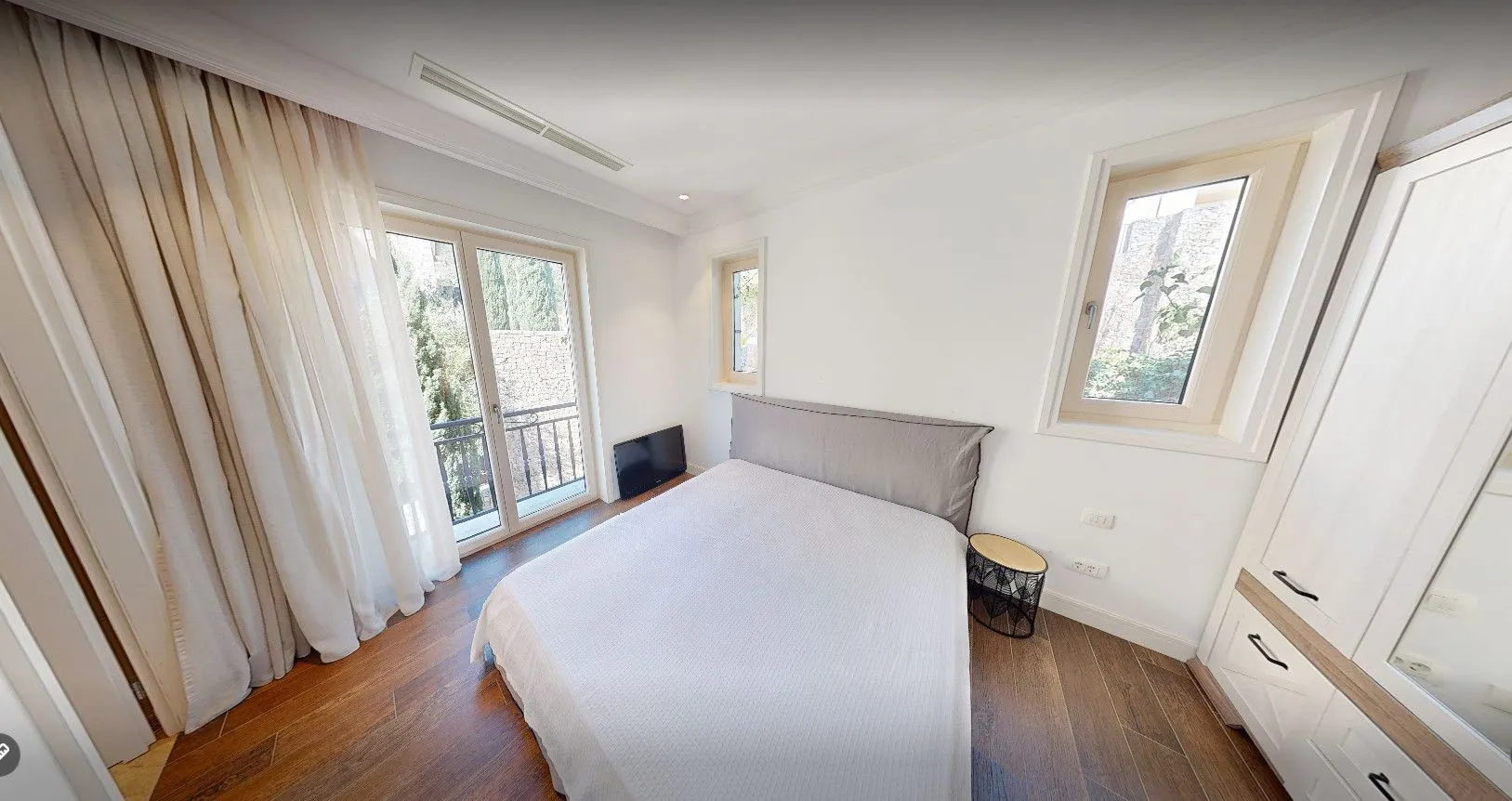 Svjetla spavaća soba sa bračnim krevetom, garderoberom i izlazom na balkon.