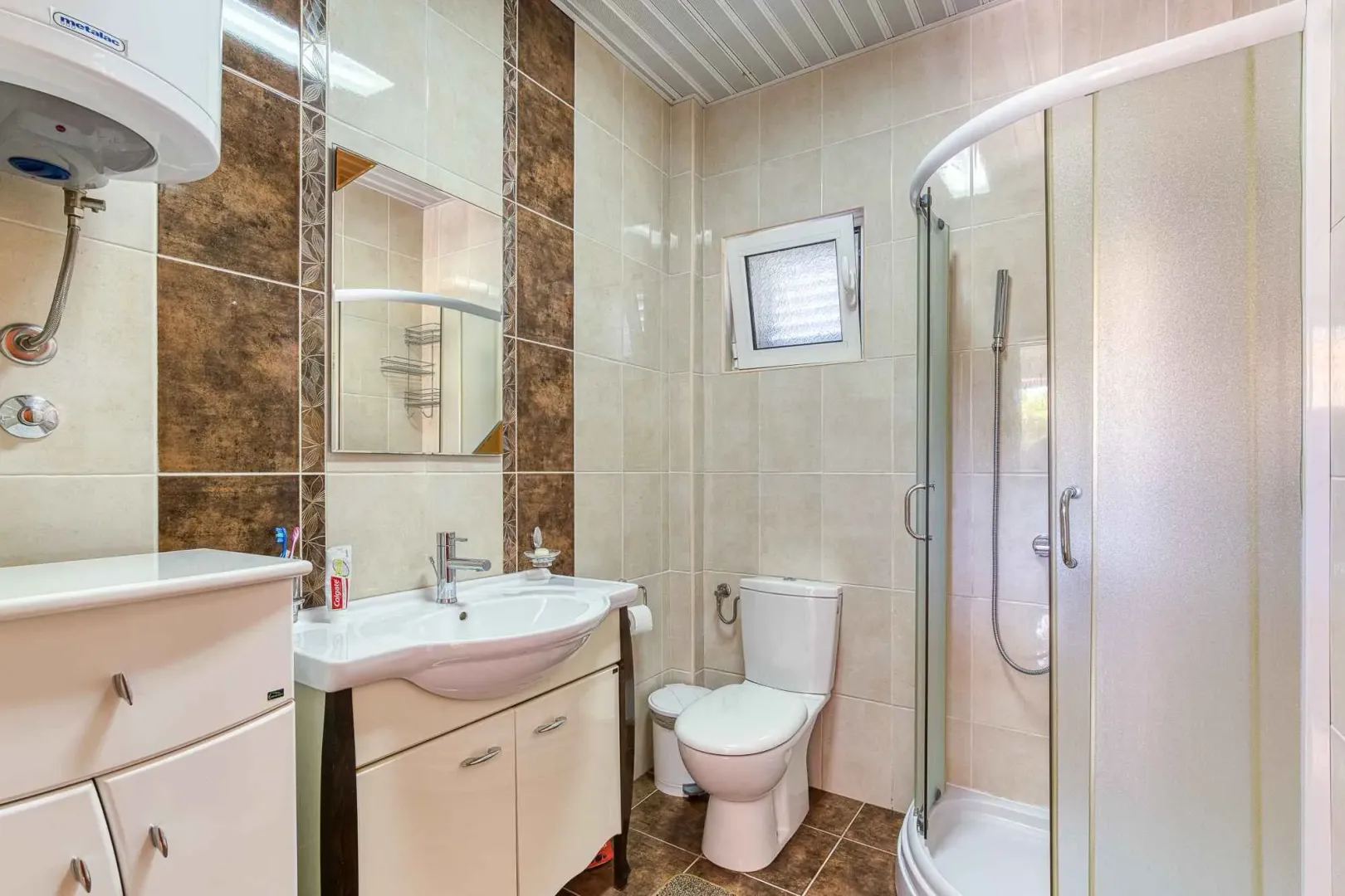 Kupatilo opremljeno umivaonikom, WC šoljom i tuš kabinom.