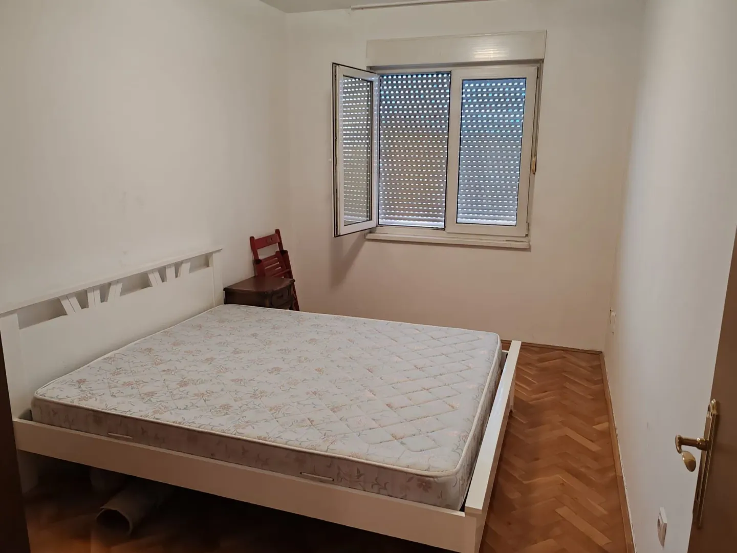 Small bedroom with a double bed, parquet flooring, and an open window.