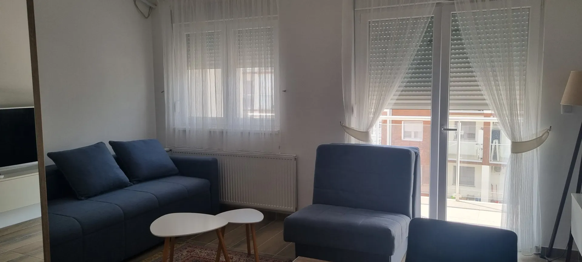 Svetao dnevni boravak sa garniturom i malim stolovima.