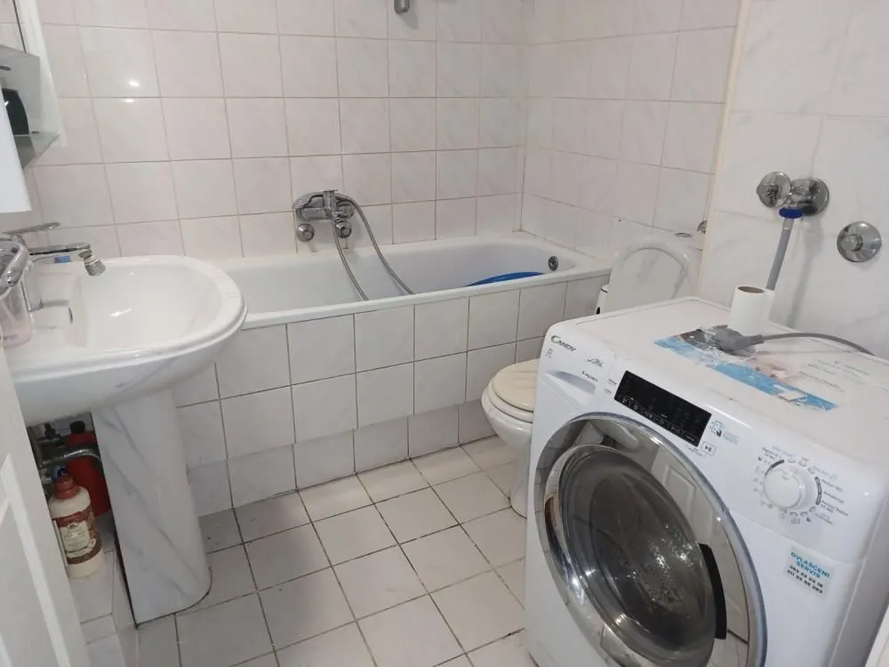 Manje kupatilo sa kadom, umivaonikom, toaletom i veš mašinom.