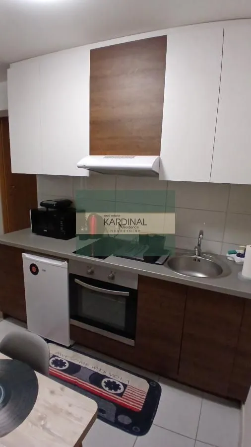 Manja kuhinja sa belim i drvenim elementima, ugradnom rernom i sudoperom.