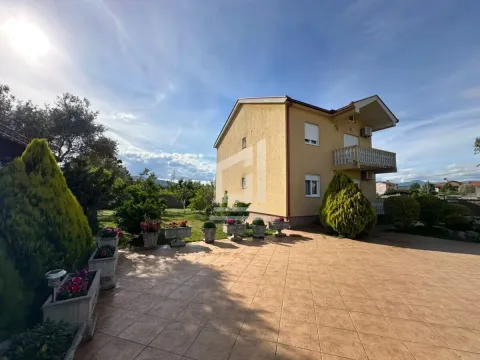 Pogled na dvorište i spoljašnjost kuće sa popločanim platoom i uređenim zelenilom. - image 2