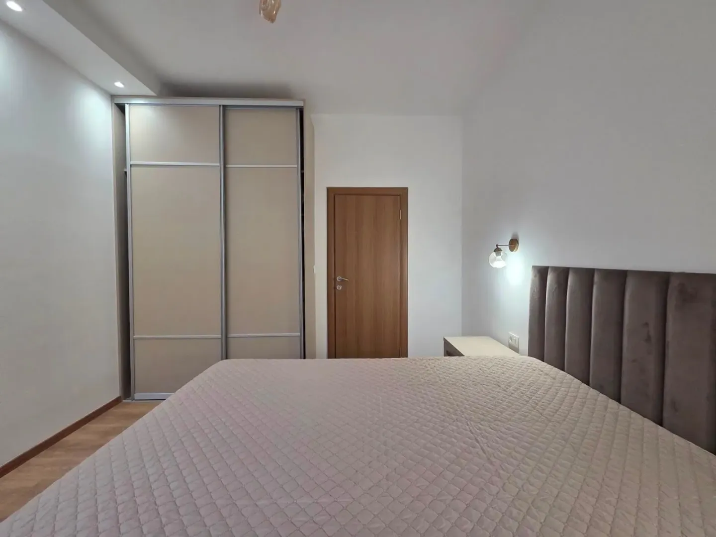 Furnished bedroom with a double bed, wardrobe, and wooden door.