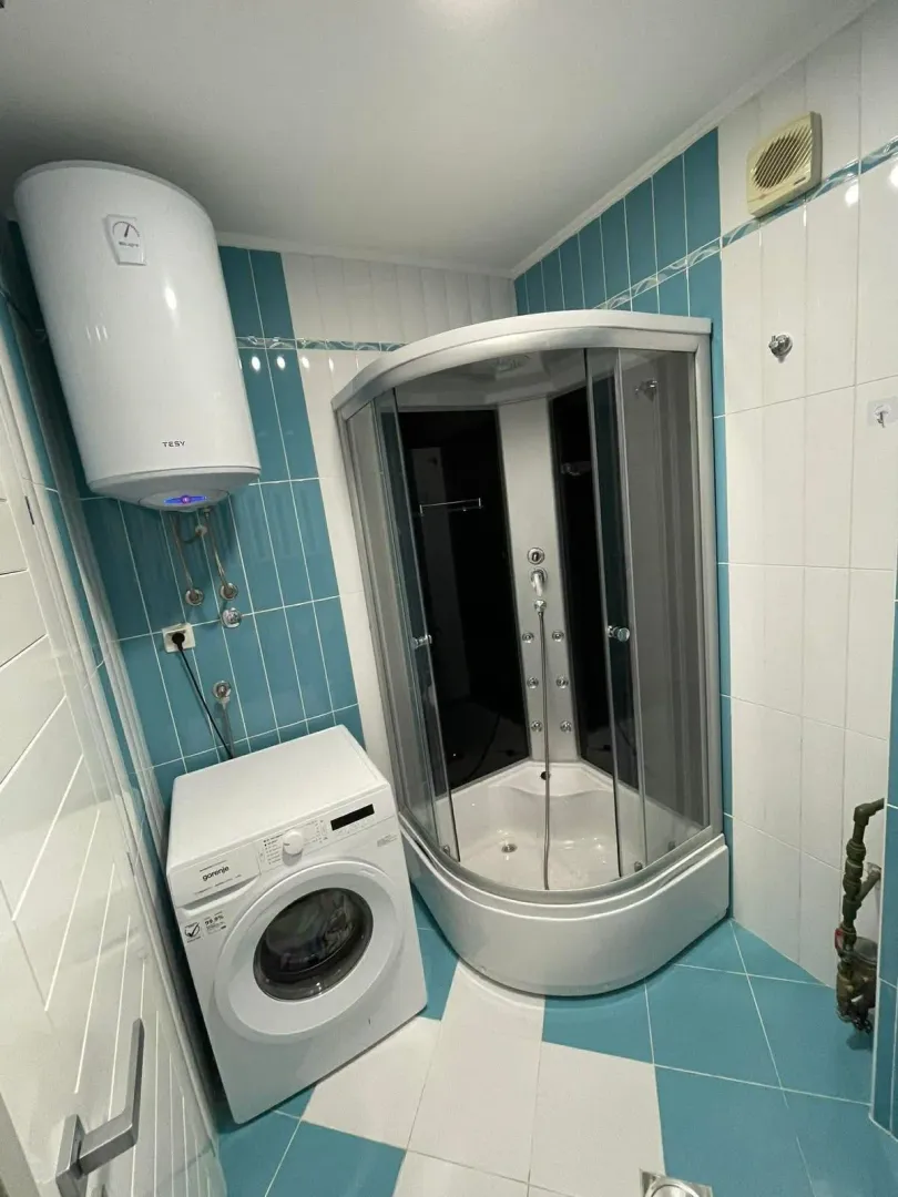 Bathroom with a shower cabin, water heater, and washing machine.