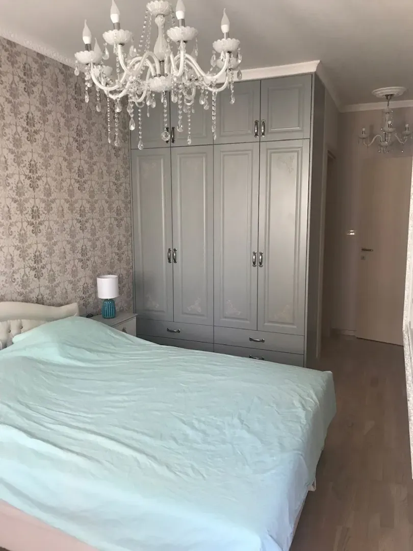Svijetla spavaća soba sa velikim sivim ormarom i ukrasnim lusterom.
