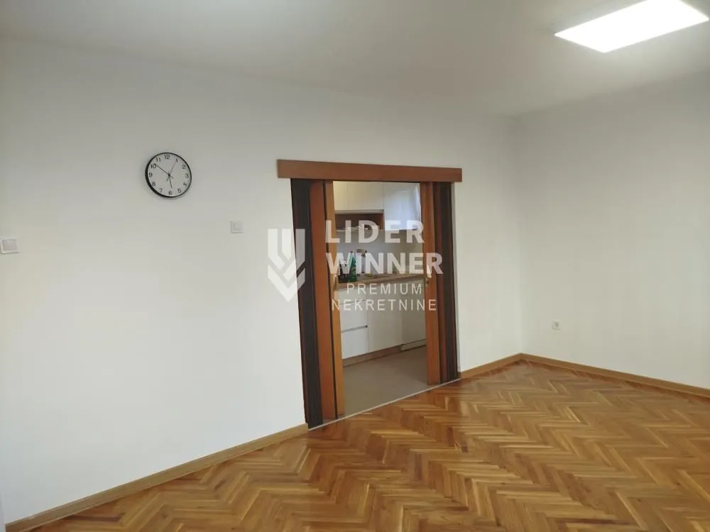 Empty room with wooden flooring and a wall clock.