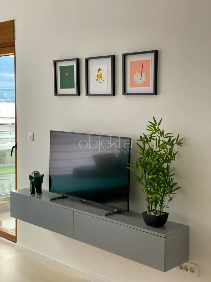 Detalj enterijera sa televizorom, komodom i slikama na zidu.