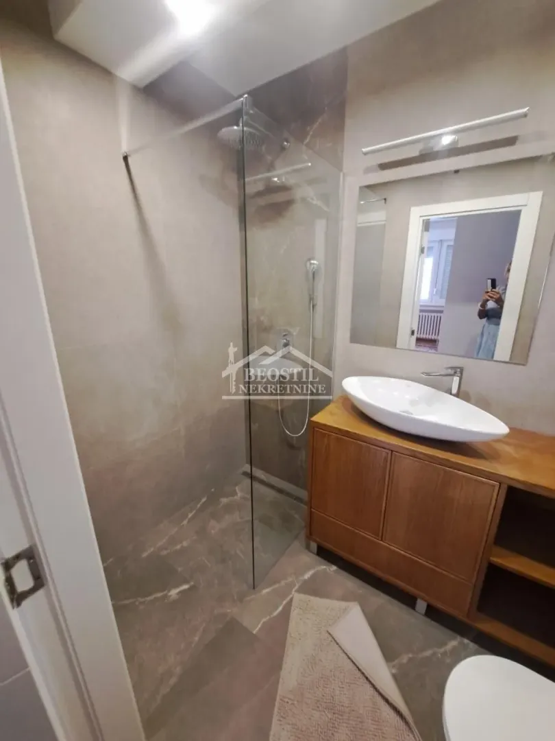 Moderno kupatilo sa tuš kabinom i drvenim ormarićem sa umivaonikom.