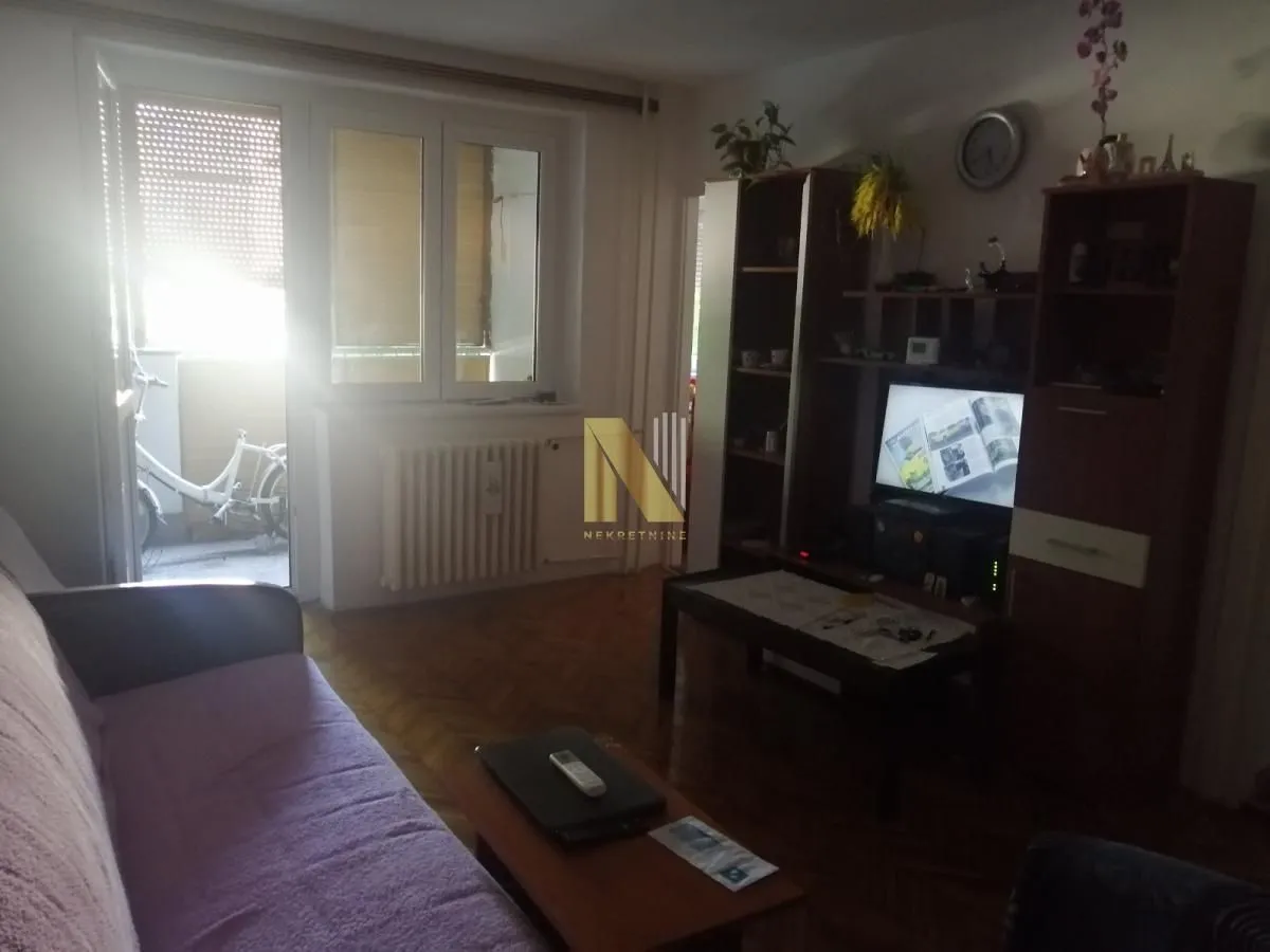 Dnevna soba sa garniturom, TV komodom i izlazom na terasu.