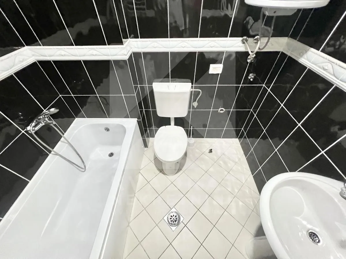 Bathroom equipped with a bathtub, washbasin, and toilet, featuring black wall tiles and light floor tiles.