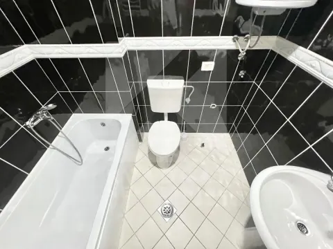 Bathroom equipped with a bathtub, washbasin, and toilet, featuring black wall tiles and light floor tiles. - image 6